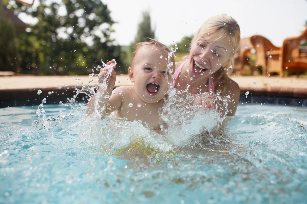 Child and adult splashing in swimming pool.