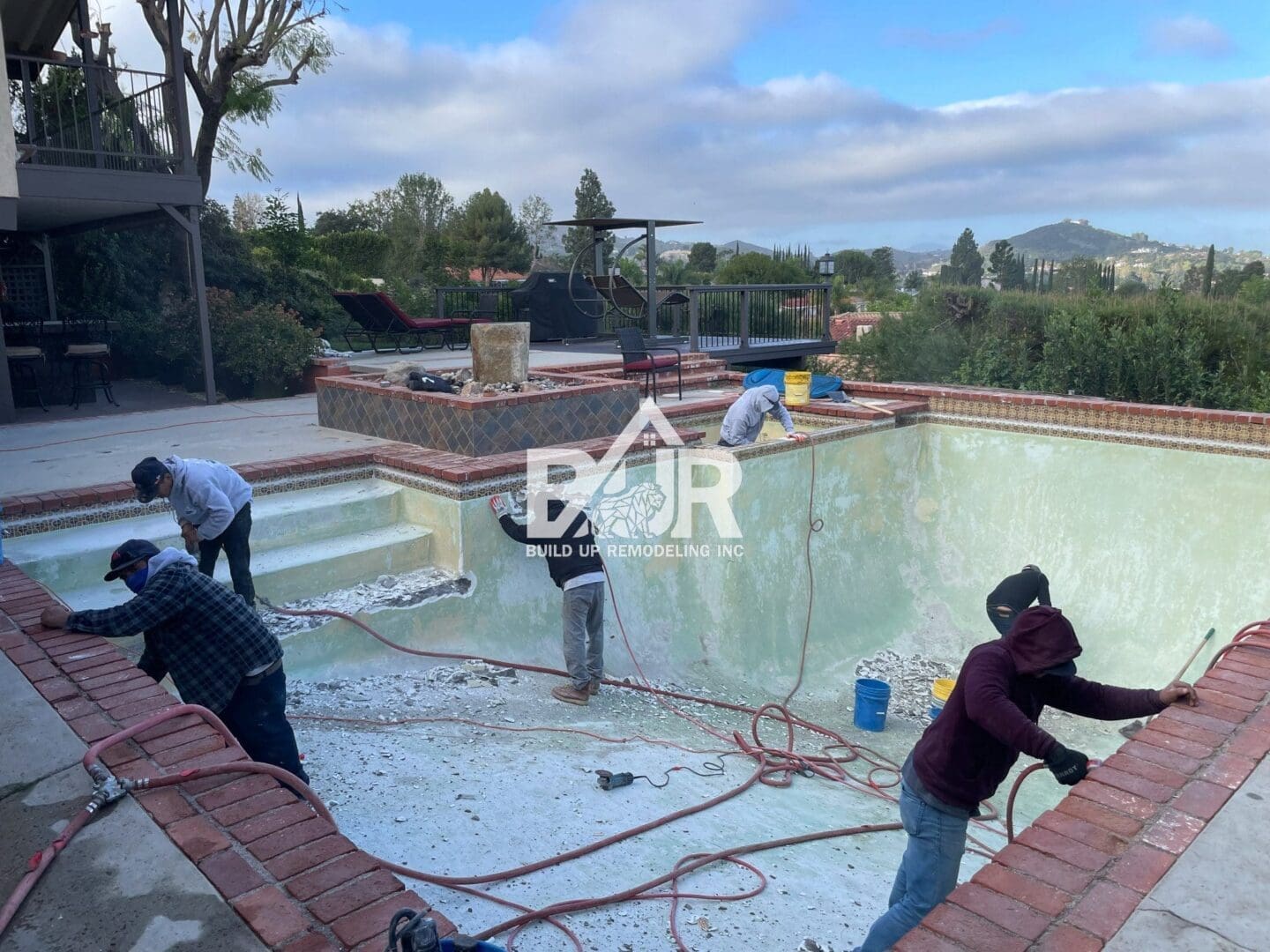 Workers renovating an empty pool with tools and equipment.