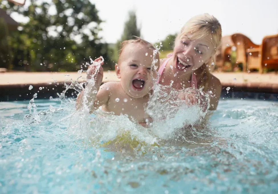 Child and adult splashing in swimming pool.